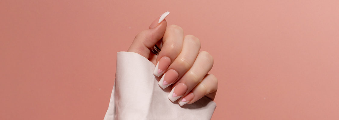 Gros plan d’une main manucurée avec french et nail art en forme de cœur sur fond rose doux, symbolisant une beauté des ongles sûre et sans TPO.